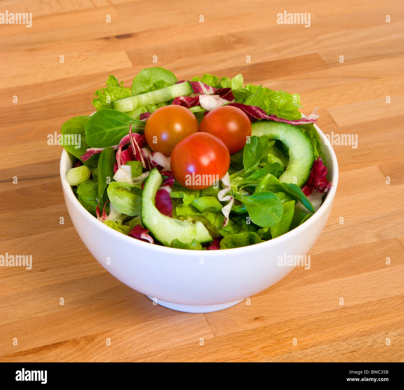 Cibo, verdure, insalata, bianco ciotola di miste di foglia verde con insalata di pomodori e cetrioli su un tavolo di legno alto. Foto Stock