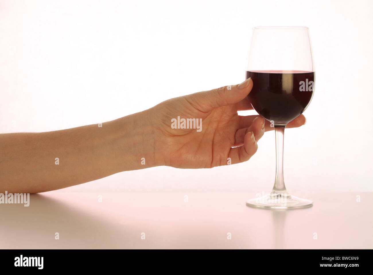 La mano di raggiungere per un bicchiere di vino rosso (magenta tonica) Foto Stock