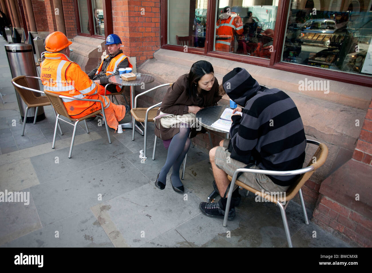 Lavoratori edili e turisti seduto fuori da un bar a London St Pancras International Train Station. DAVID MANSELL Foto Stock