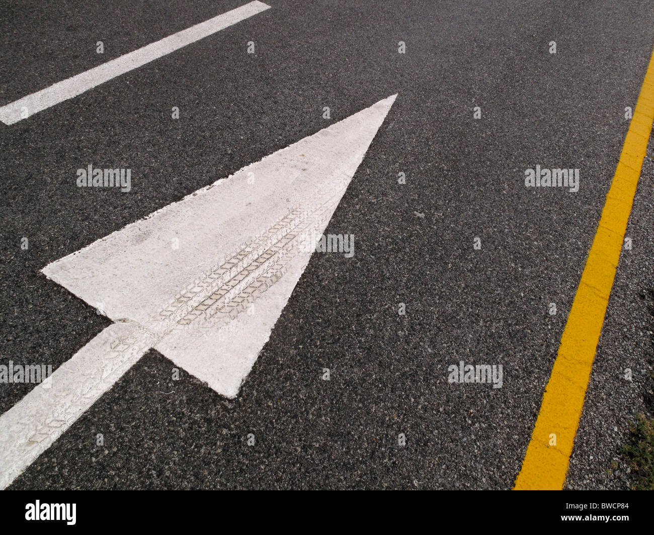 Freccia bianca sulla strada che indica la direzione per il traffico a seguire. Marchio di pneumatici integrati in vernice sulla freccia. Foto Stock