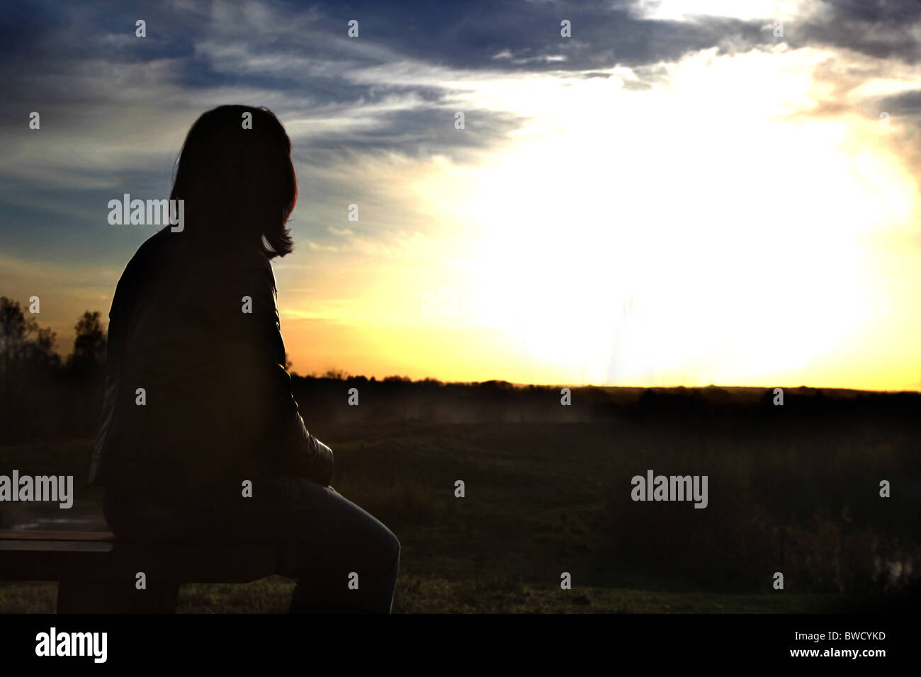Vista posteriore di una donna seduta a guardare verso un tramonto Foto Stock