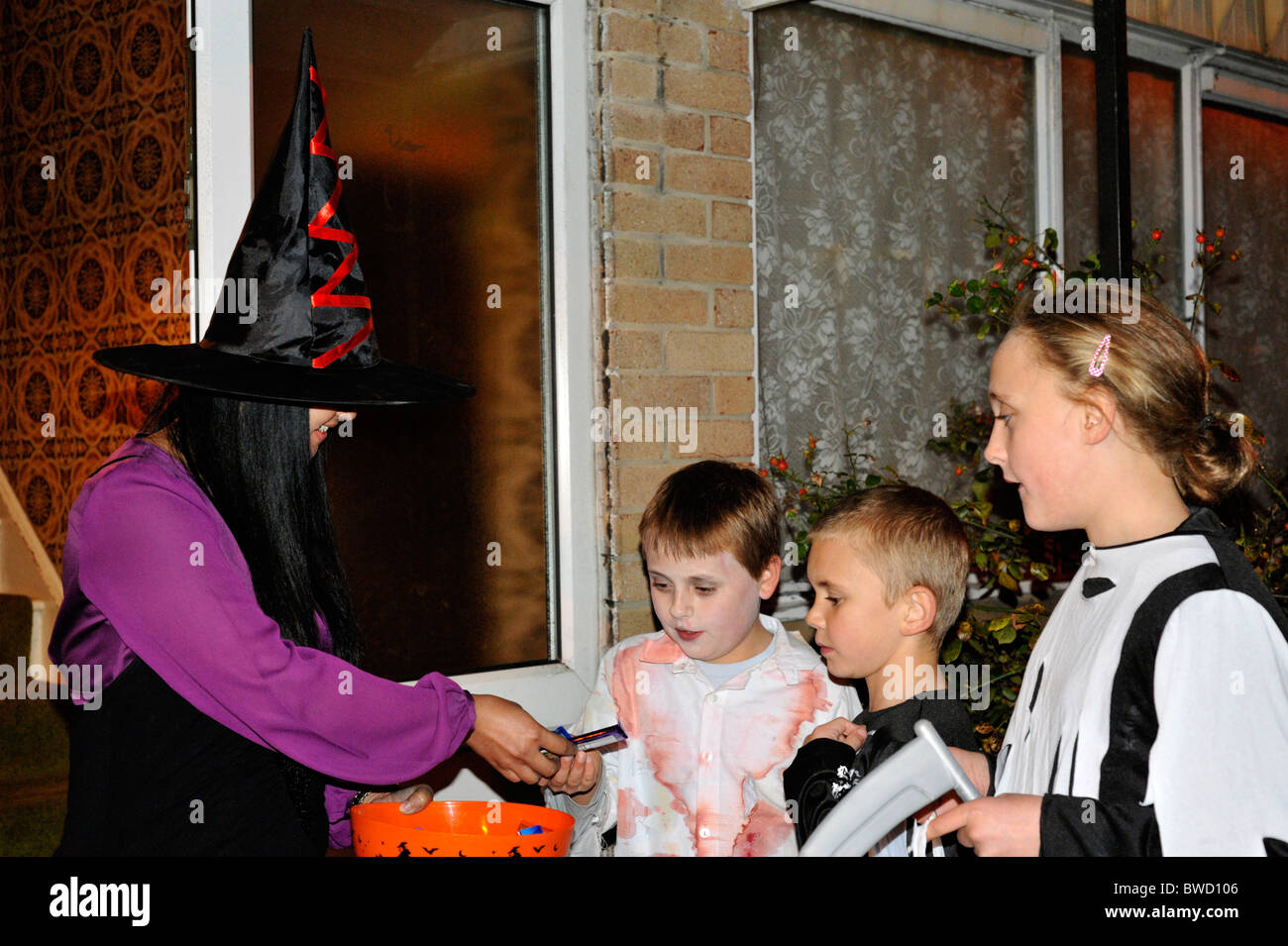 Donna vestita come una strega dare ai bambini caramelle e dolci durante il periodo di halloween dolcetto o scherzetto Foto Stock