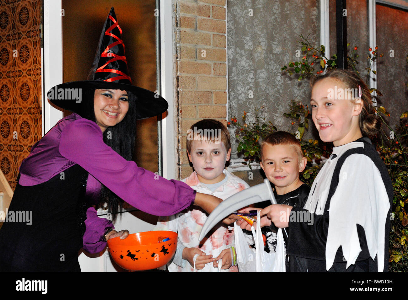 Donna vestita come una strega dare ai bambini caramelle e dolci durante il periodo di halloween dolcetto o scherzetto Foto Stock