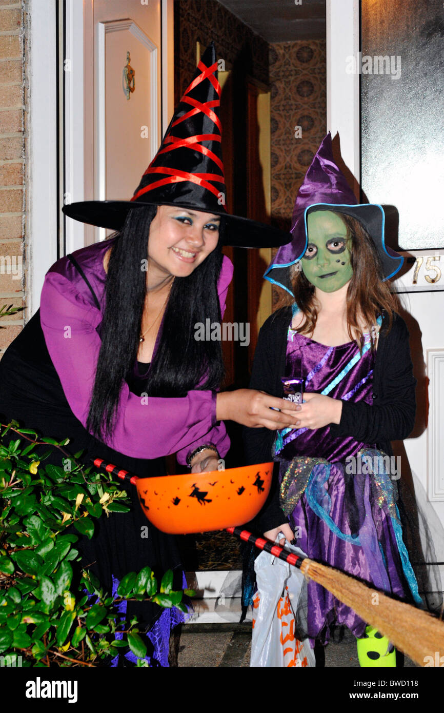 Donna vestita come una strega dando un bambino caramelle e dolci durante il periodo di halloween dolcetto o scherzetto Foto Stock