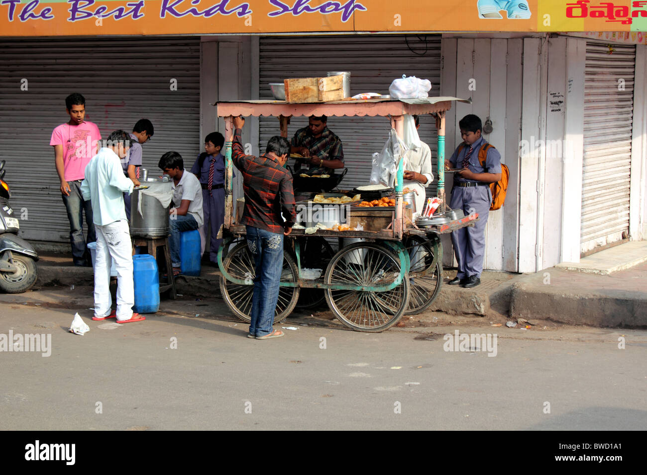 Pressione di stallo di strada in India di vendita di alimenti con i giovani e scolari in uniforme di mangiare Foto Stock