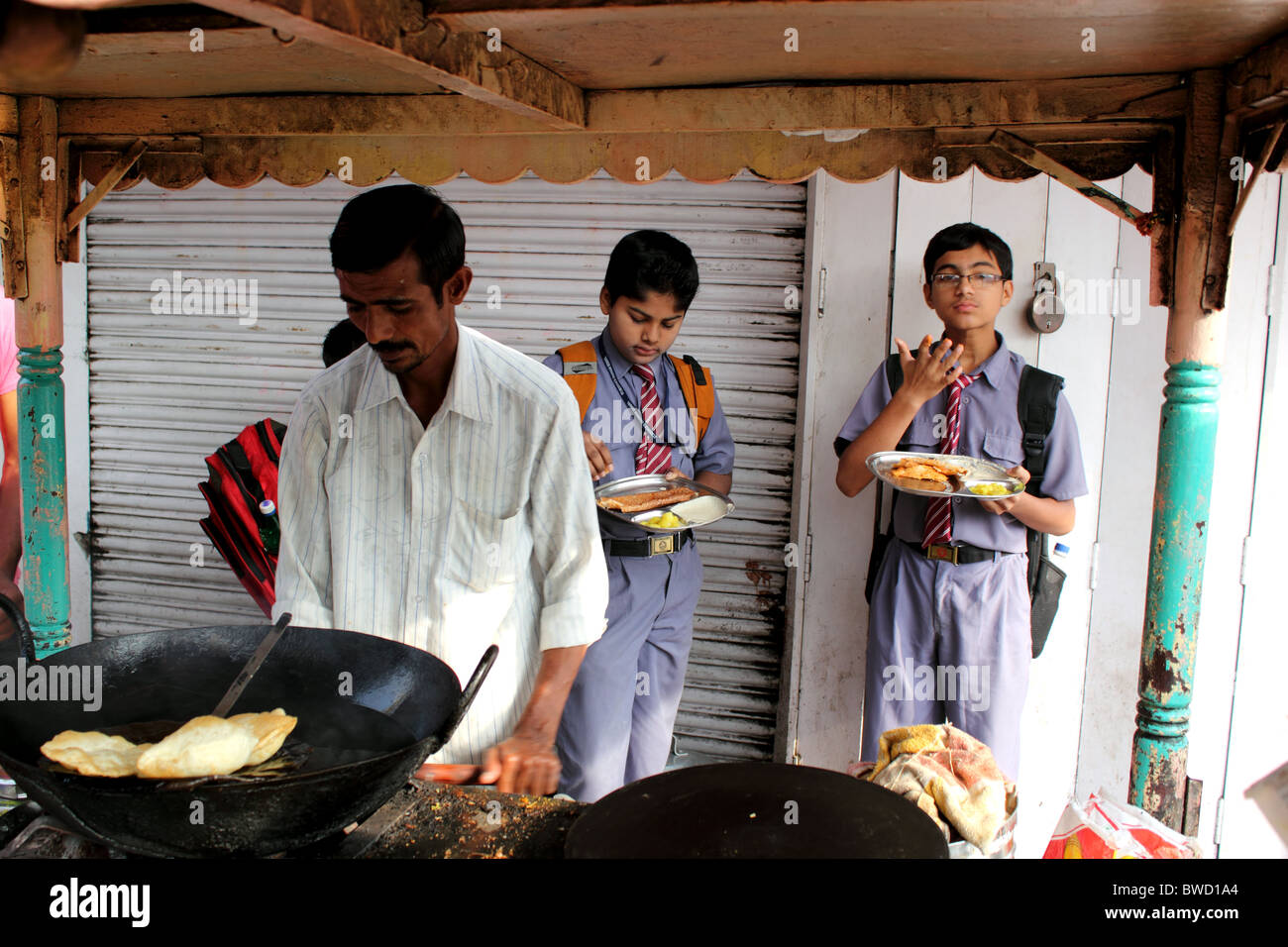 Pressione di stallo di strada in India di vendita di alimenti con i giovani e scolari in uniforme di mangiare Foto Stock