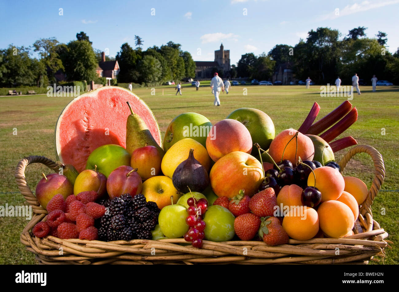 Cestello di deliziose coltivati localmente sano fresco frutta estiva accanto a Benenden verde villaggio con partita di cricket in gioco Kent REGNO UNITO Foto Stock