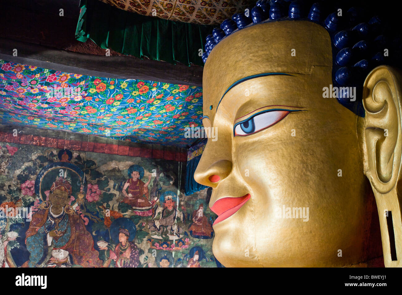 Vista ravvicinata della testa del golden statua del Buddha con le antiche pitture murali in background. Monastero di Shey, Ladakh, India. Foto Stock