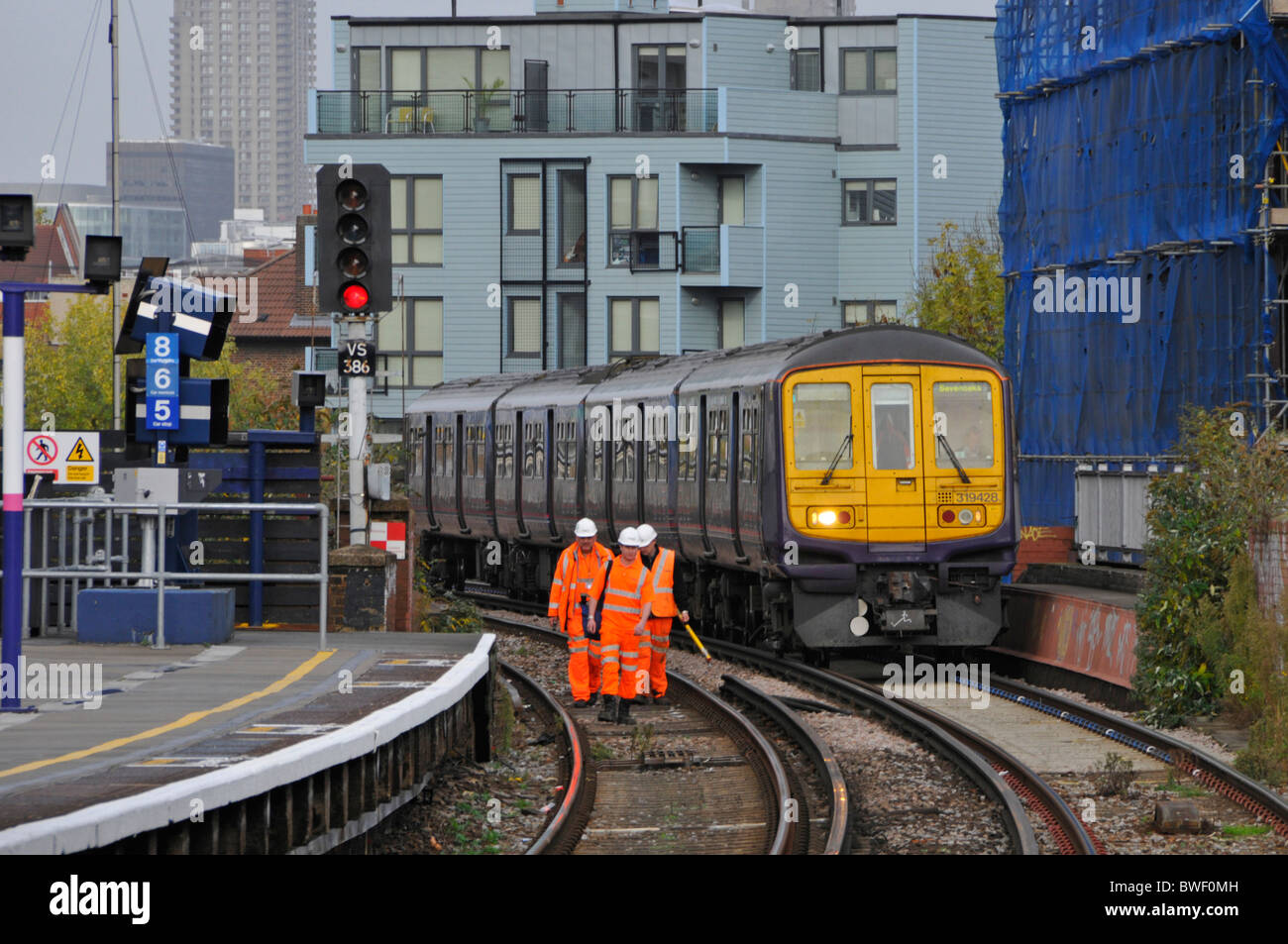 Manutenzione infrastrutture ferroviarie lavoratori di equipaggio in giacche di alta visibilità & Treno a cappello che corre sulla terza pista elettrica Sud Londra Inghilterra Regno Unito Foto Stock