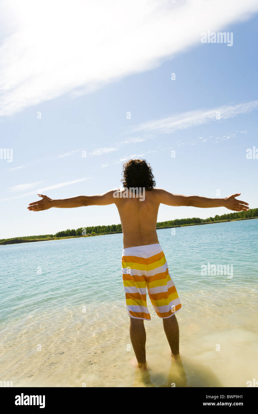 Vista posteriore del giovane uomo in piedi in acqua blu e divertirsi con le braccia tese su caldo giorno d'estate Foto Stock