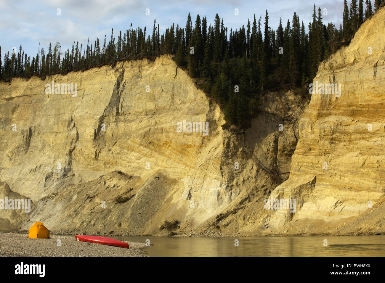 Il Camp, tenda e canoa su una barra di ghiaia, alta cut bank, fiume cliff, erosione, dietro, superiore Liard River, Yukon Territory, Canada Foto Stock