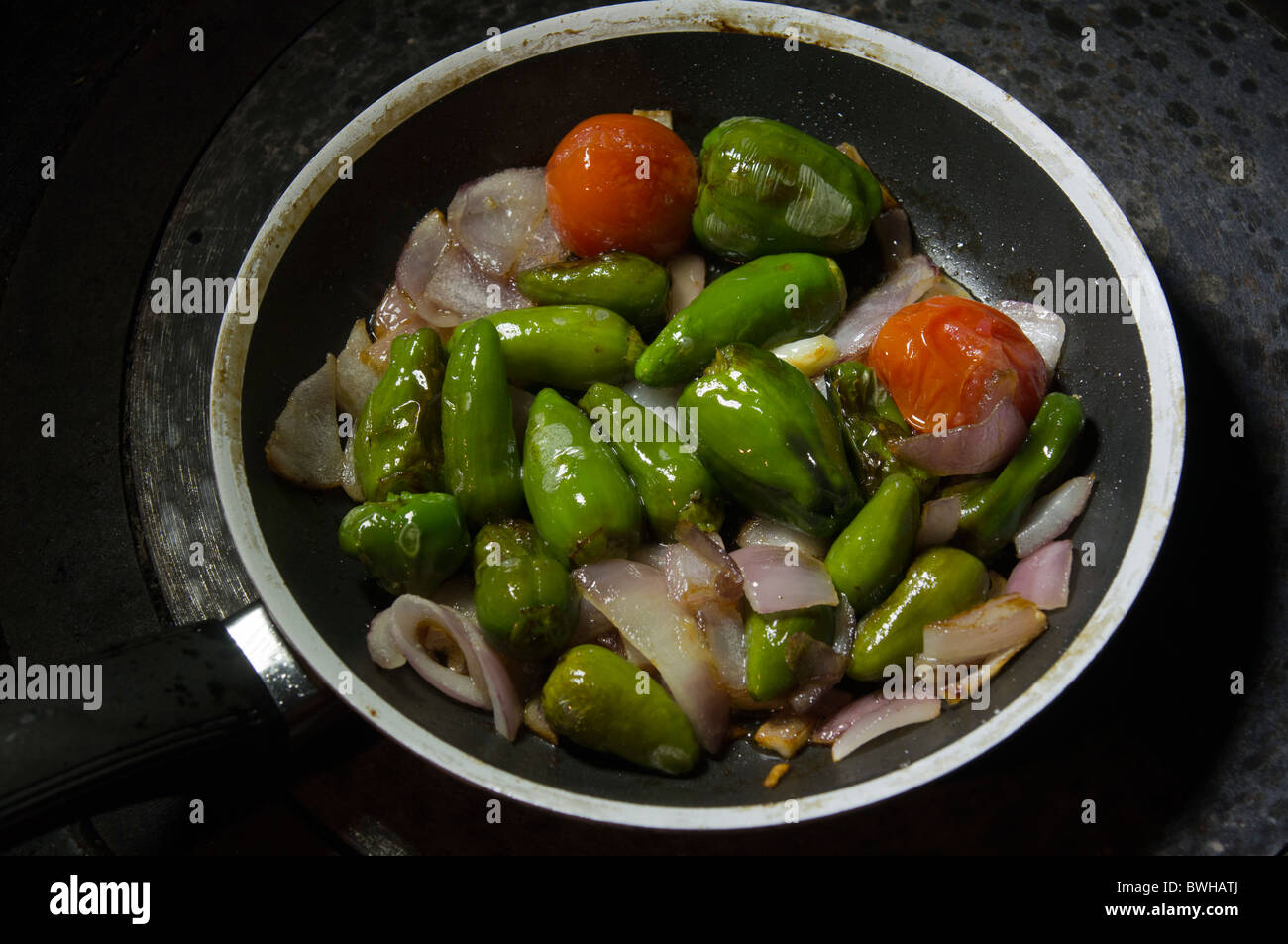 La cottura di piccoli dolci peperoni verdi,cipolla rossa e pomodorini in una padella con olio di oliva. Foto Stock