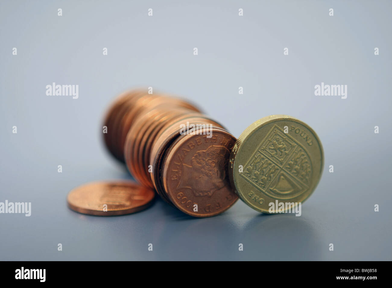 Una fila di sterling 1p delle monete in euro e sterline di 1 gettone tutti su estremità con un 1p coin in piano sulla superficie Foto Stock