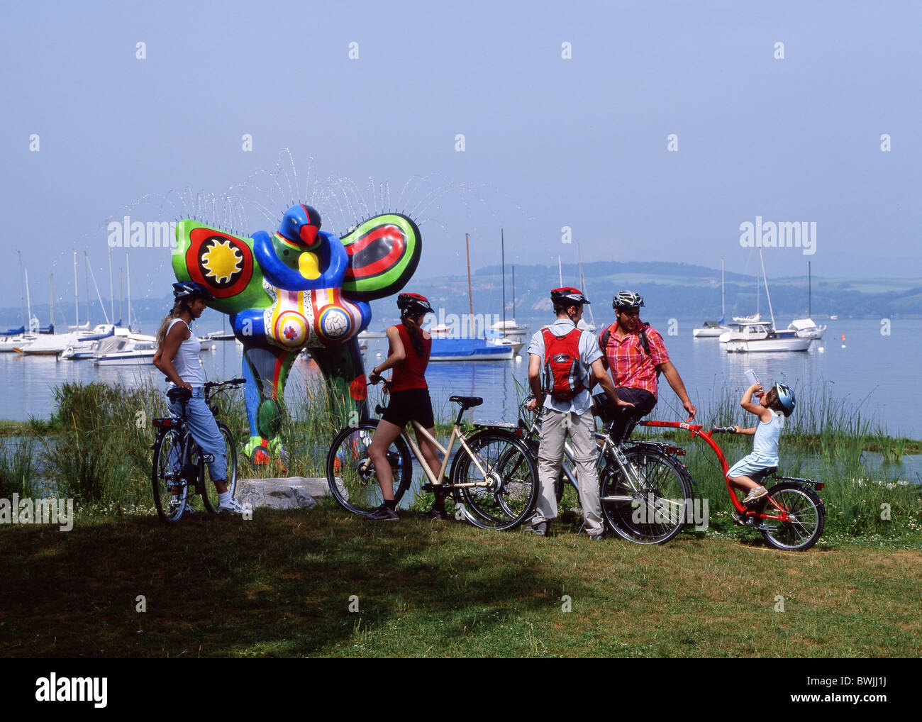 Tour in bicicletta Famiglie gruppo riva lago Murtensee lago di Morat arte plastica specialità di Niki de Saint Phalle statua Foto Stock