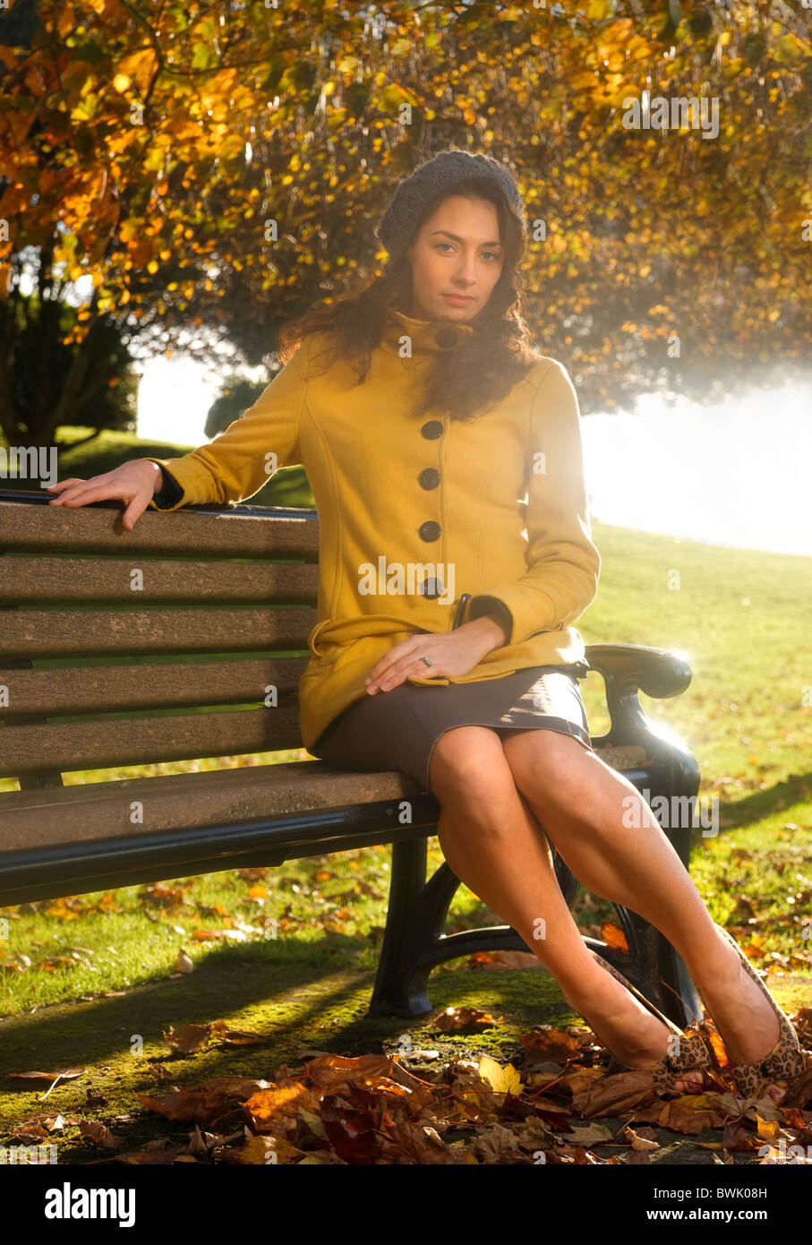 Donna in posa su una panchina nel parco che indossa lo stile anni cinquanta abbigliamento sotto una tettoia di albero in autunno colori foglia Foto Stock