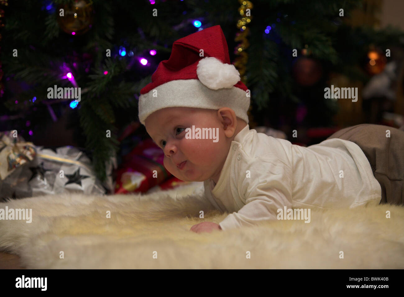 Little baby boy vestiti come santa claus nella parte anteriore di un albero di natale con doni. Foto Stock