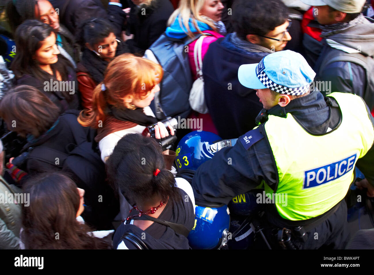 Londra, Regno Unito. Un funzionario di polizia lo spinge attraverso la folla per fornire elmetti antisommossa ai colleghi nel corso di una protesta studentesca contro pianificare Foto Stock
