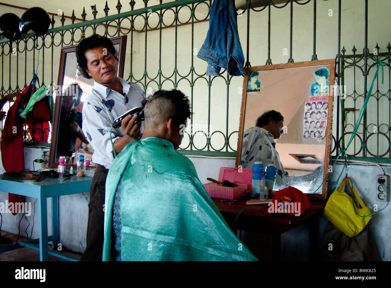 In un tradizionale villaggio mercato di Bali, Indonesia, un barbiere dà un taglio di capelli a un cliente. Foto Stock