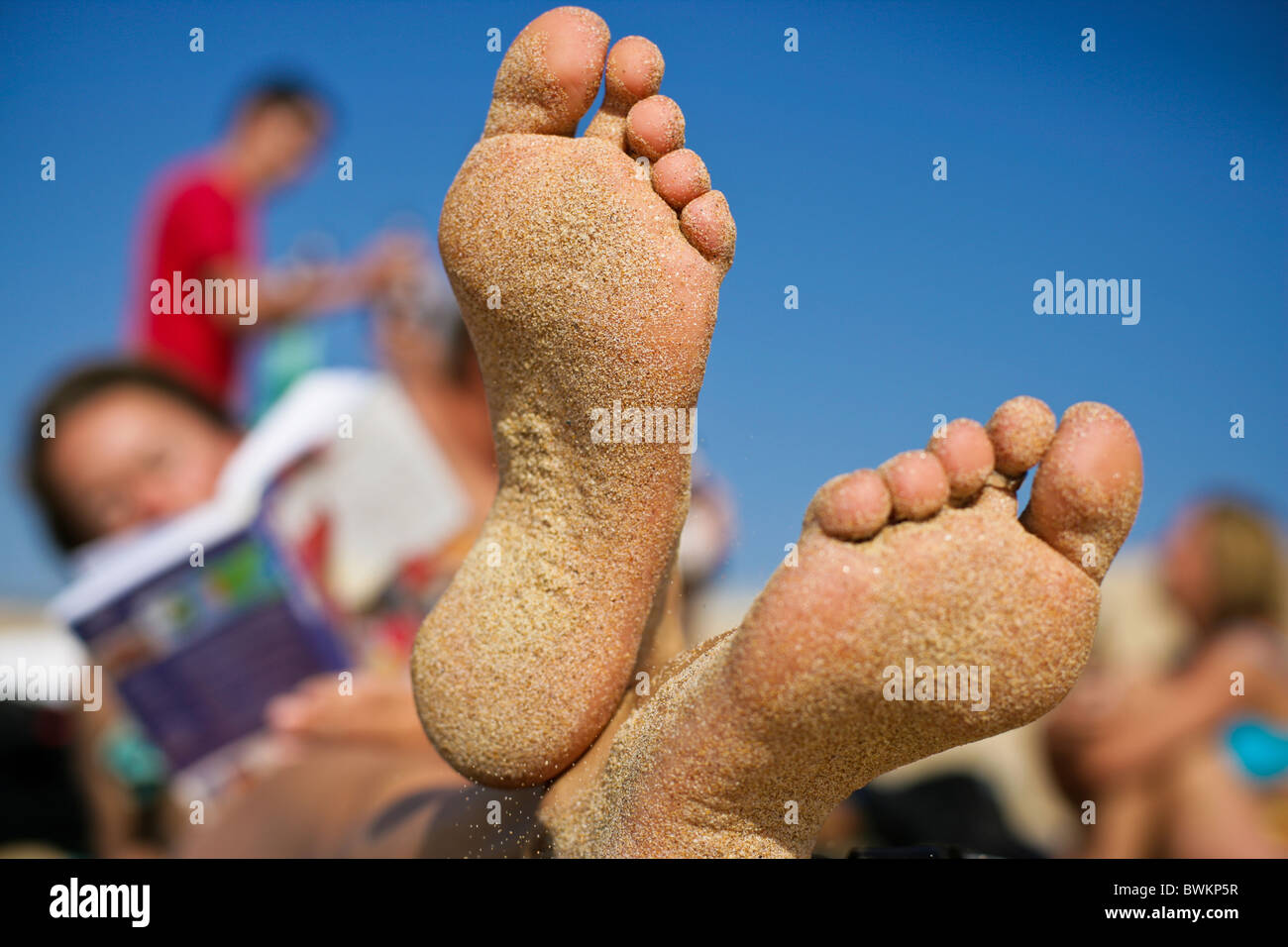 Piedi di sabbia sulla spiaggia. donna si rilassa con libro in vacanza con gli amici Foto Stock