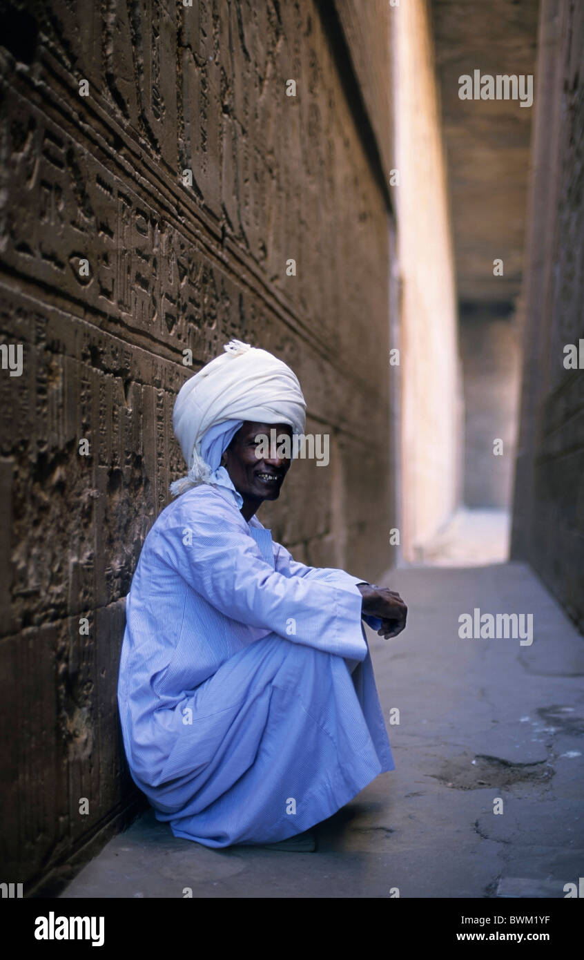 Egyptian uomo seduto contro una parete del Tempio di Edfu, Edfu, Egitto. Foto Stock