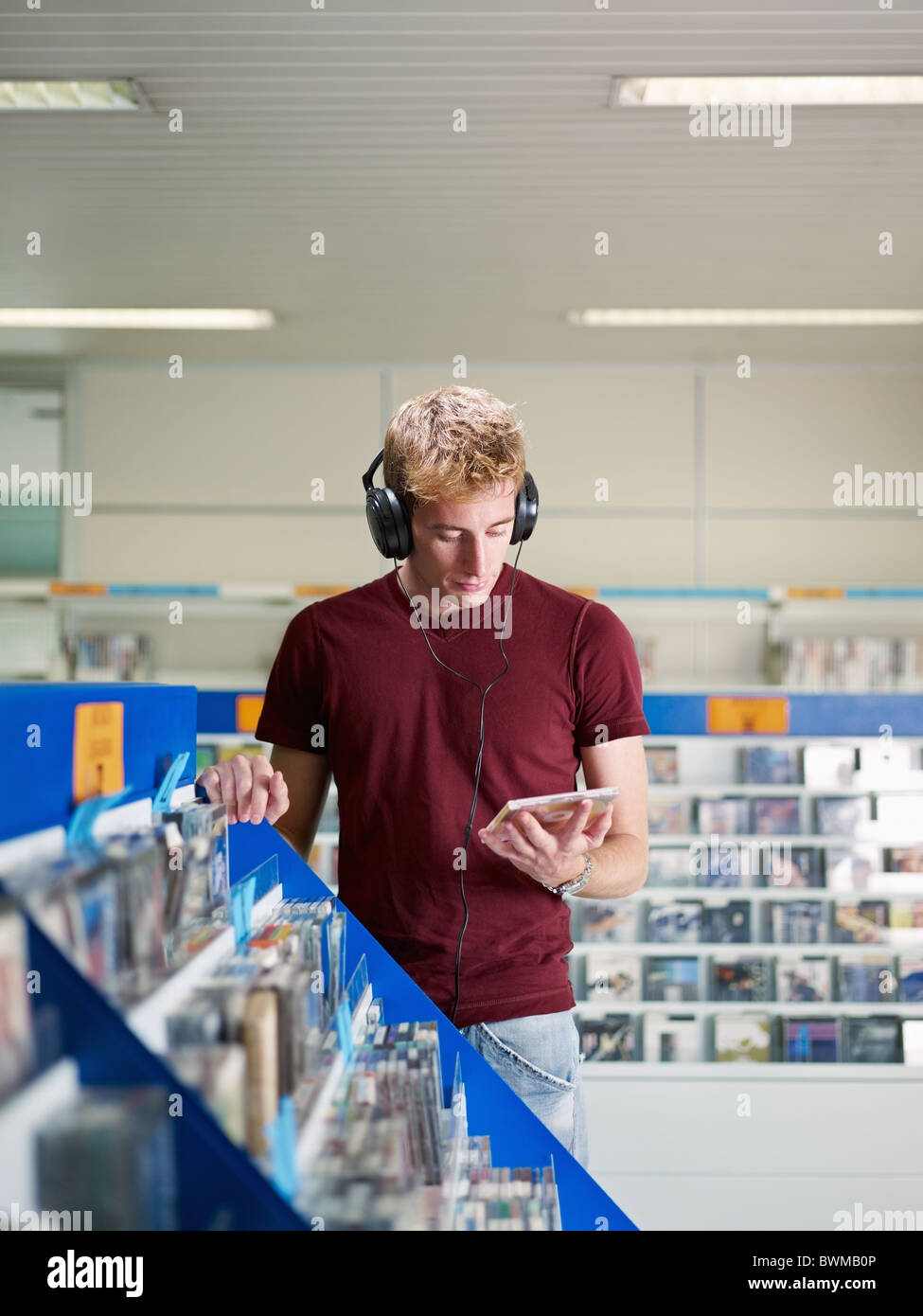 Uomo caucasico con le cuffie, scegliere cd nel negozio di musica. Forma verticale, vista frontale, vita, spazio di copia Foto Stock