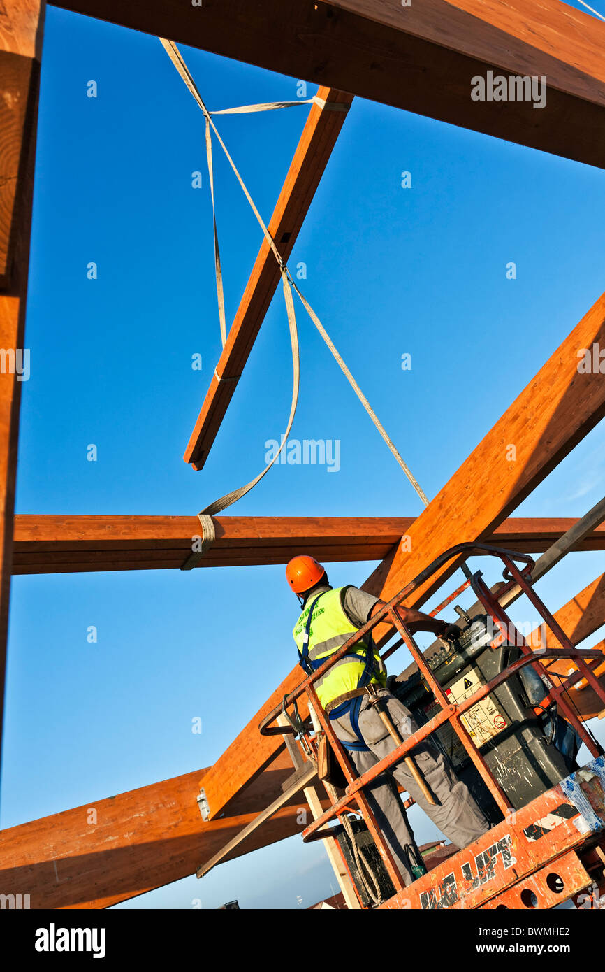 Workman la costruzione di una struttura di telaio di travi lamellari su un cherry picker Foto Stock