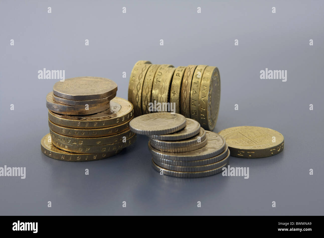 Due risme di sterling monete di fronte a una fila di £ 1 monete su estremità con un £1 moneta caduta Foto Stock