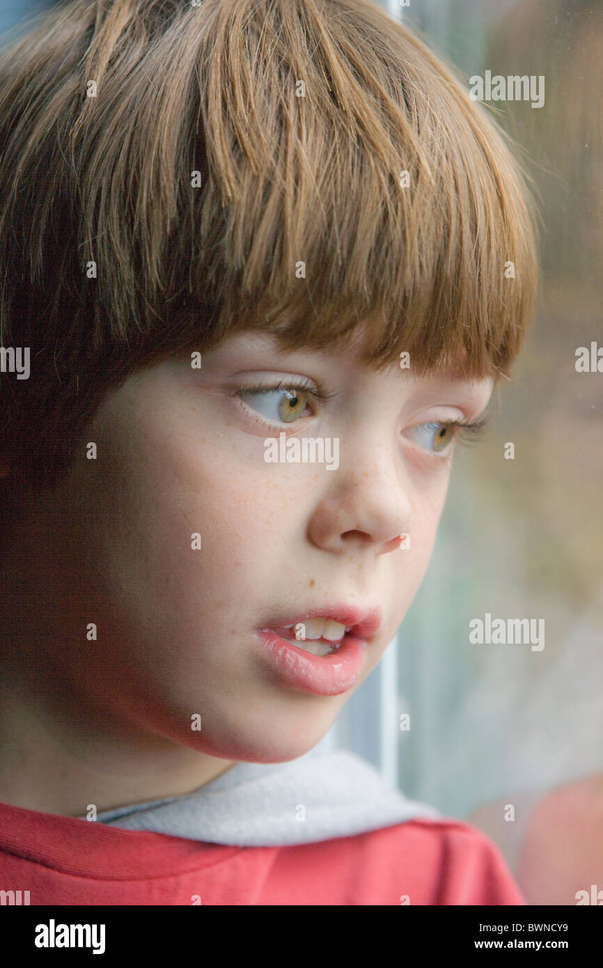 Bambino di otto anni con espressione preoccupata guardando fuori della finestra. Foto Stock