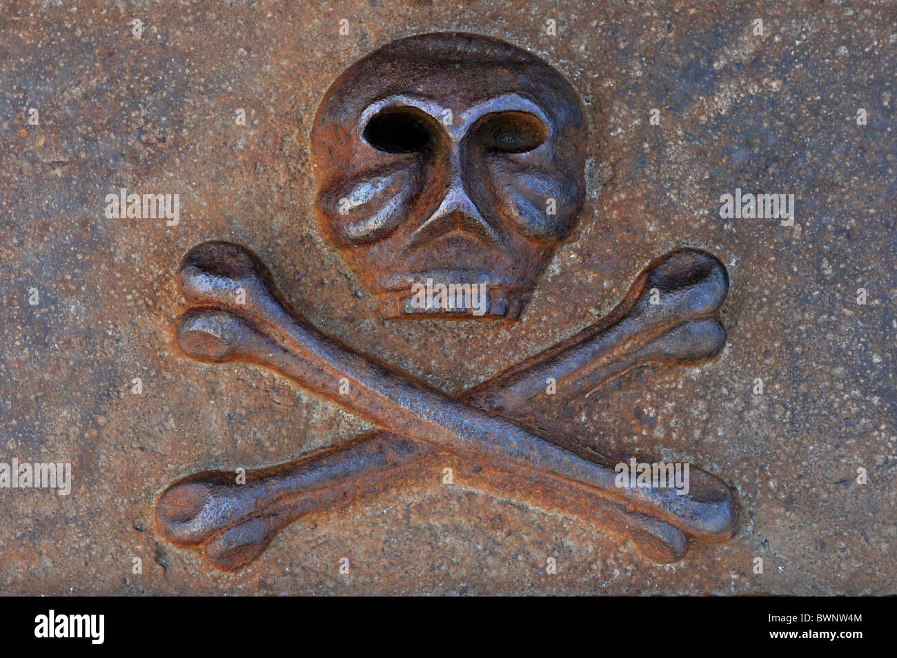 Rusty teschio umano con le ossa incrociate colato dal pericolo di ferro e simbolo di morte Foto Stock