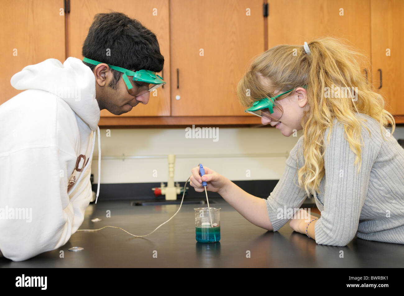 Gli studenti che indossa gli occhiali di protezione mentre si fa un esperimento di scienza di misurazione della temperatura di una reazione chimica Foto Stock