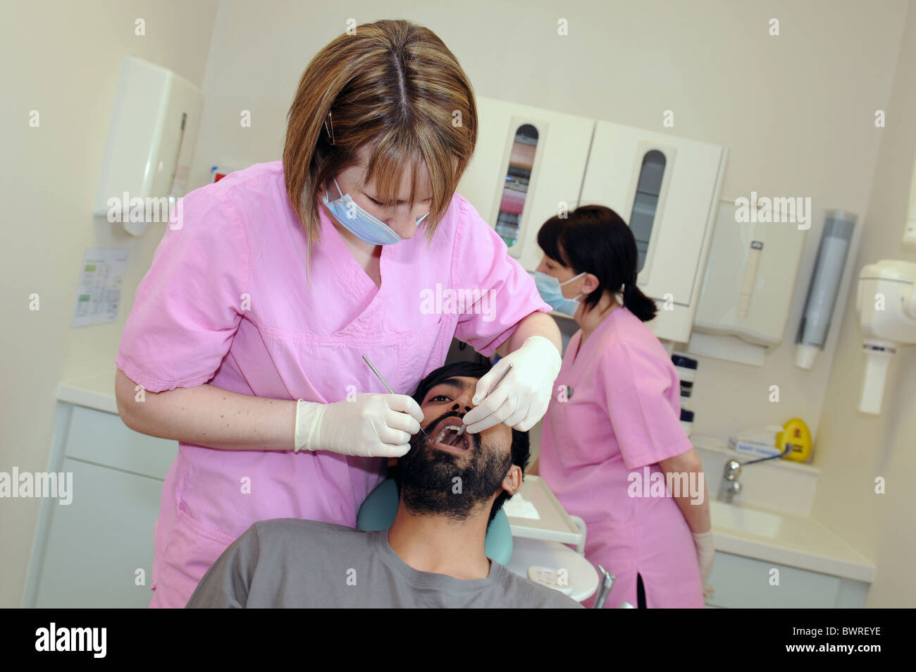 Un asiatico paziente di sesso maschile avente denti di un esame da parte di una femmina di dentista in un NHS chirurgia dentale Foto Stock