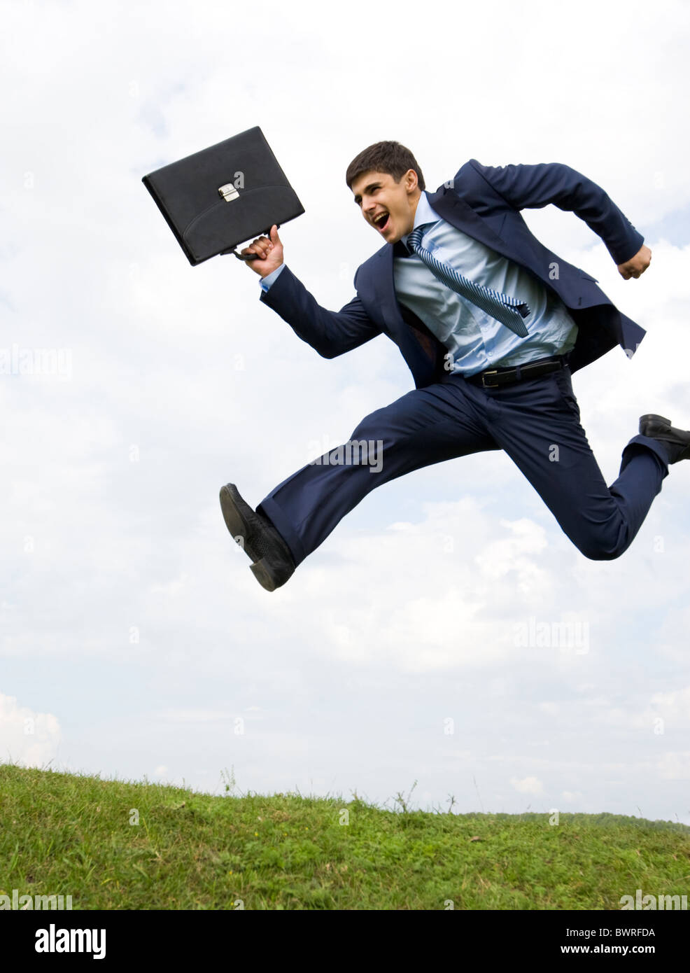 Ben vestito leader saltando su erba verde con cielo nuvoloso a sfondo Foto Stock
