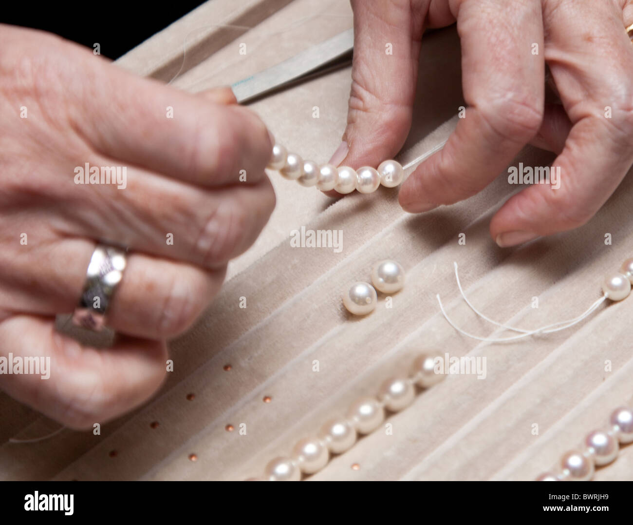 Chiudere la mano gioielliere stringing perle su una collana Foto Stock
