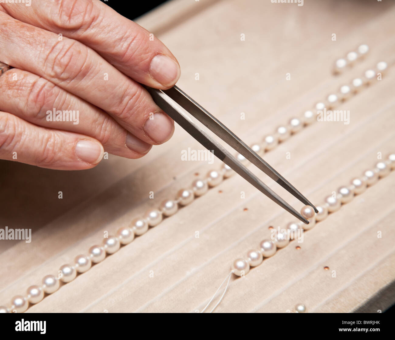 Chiudere la mano gioielliere stringing perle su una collana Foto Stock
