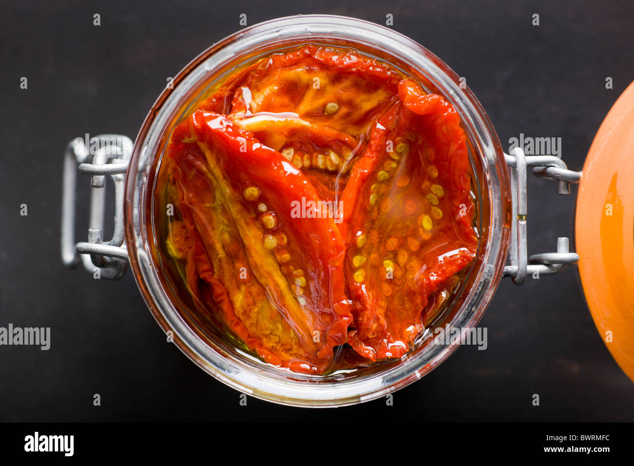 Un vaso di vetro riempito con Sun-Dried pomodori e olio di oliva su uno sfondo nero. Foto Stock