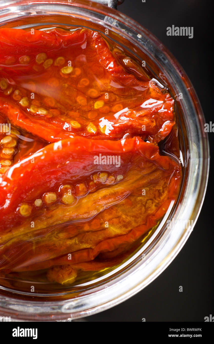 Un vaso di vetro riempito con Sun-Dried pomodori e olio di oliva su uno sfondo nero. Foto Stock