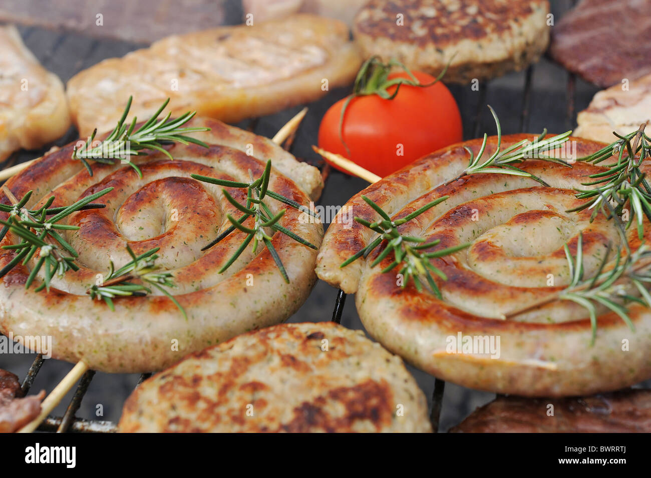 La cottura della carne sul barbecue all'aperto. Spirale salsicce Cumberland sono coperti con rametti di rosmarino. Foto Stock