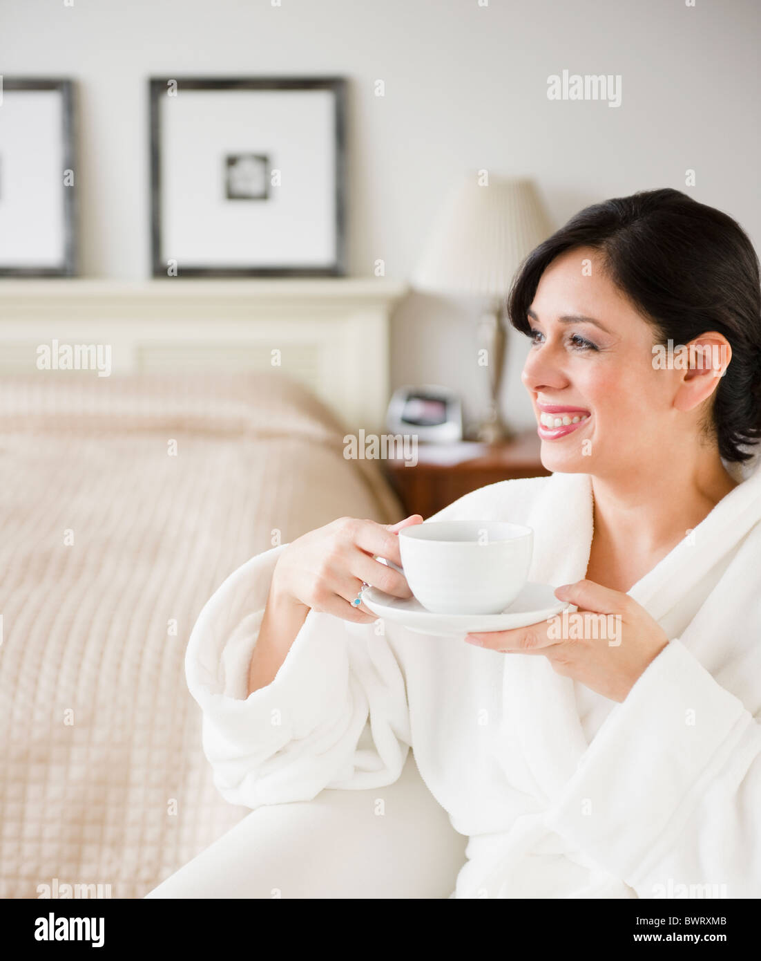 Donna ispanica in accappatoio di bere il caffè in camera da letto Foto Stock
