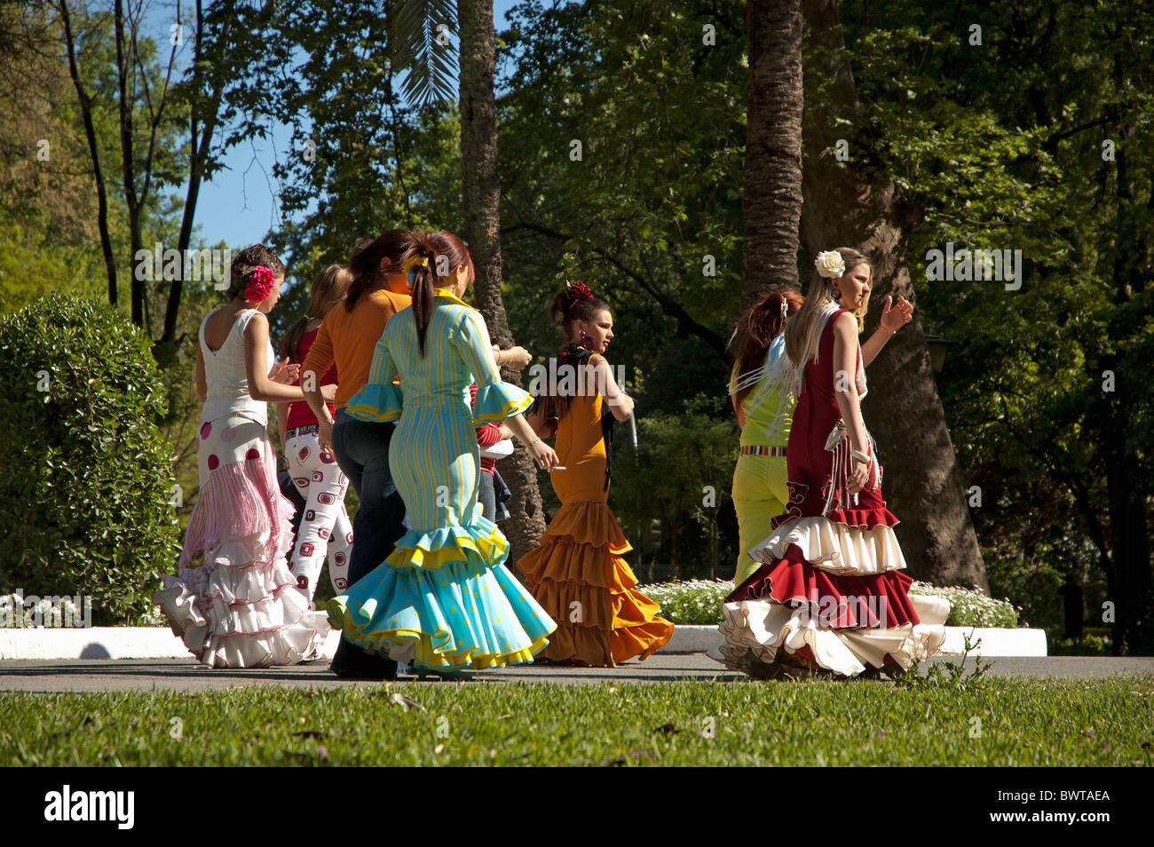 Le donne in abito di flamenco a piedi attraverso il Parco Maria Luisa verso il Siviglia Fiera di Primavera, Siviglia, Andalusia, Spagna. Foto Stock