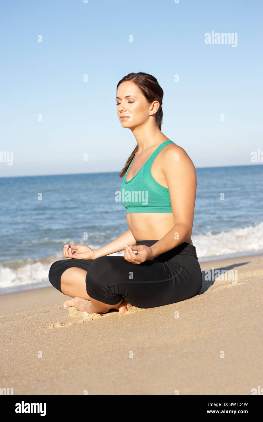 Giovane Donna Abbigliamento Fitness meditando sulla spiaggia Foto Stock
