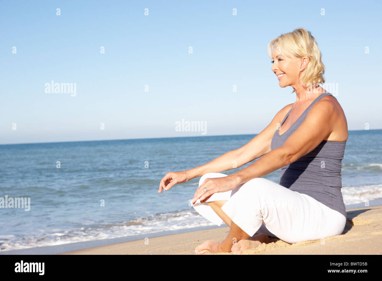 Senior Donna Abbigliamento Fitness meditando sulla spiaggia Foto Stock