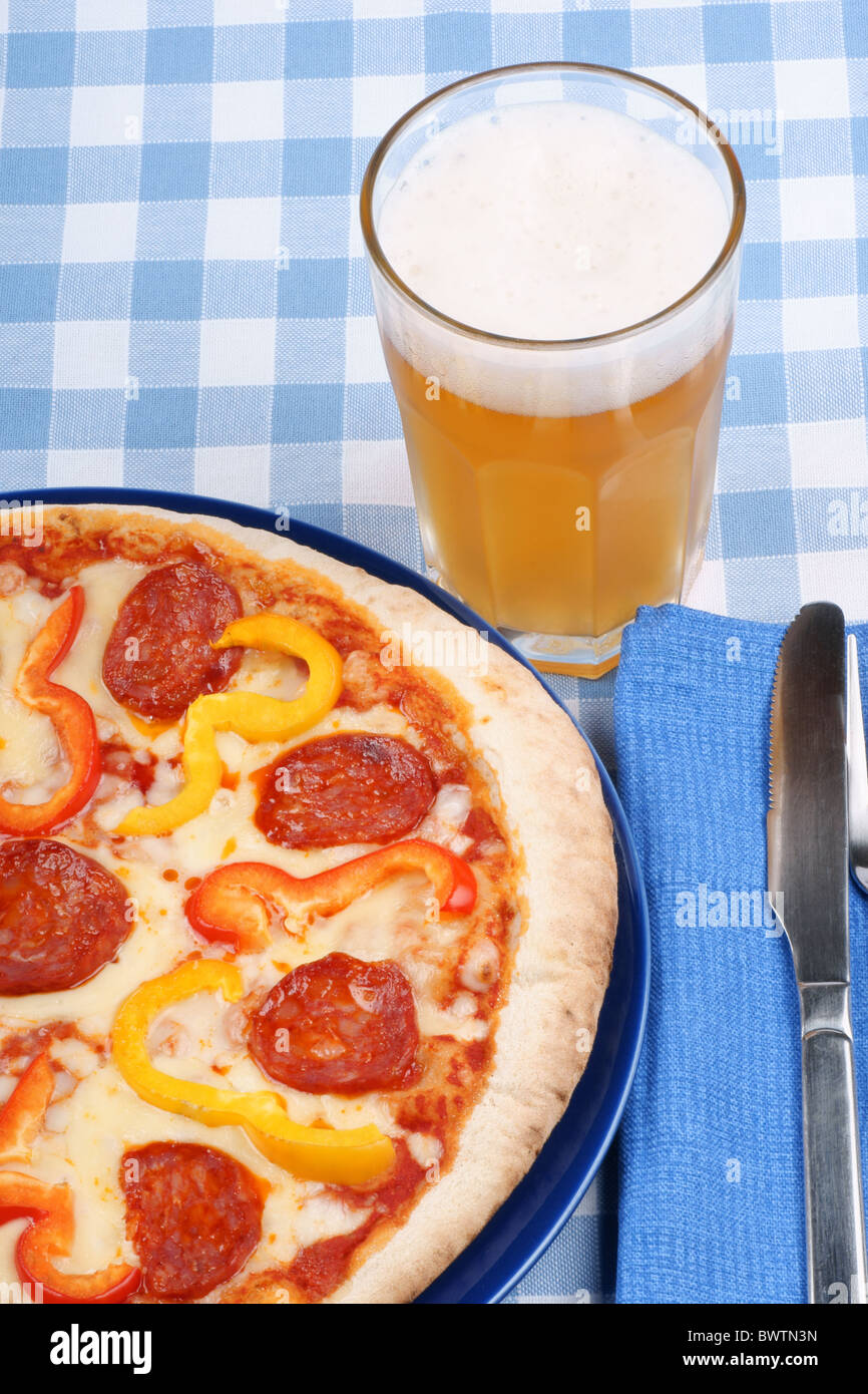 Impostare il tavolo con piccante pizza con salame e peperoni e un bicchiere di birra. Foto Stock