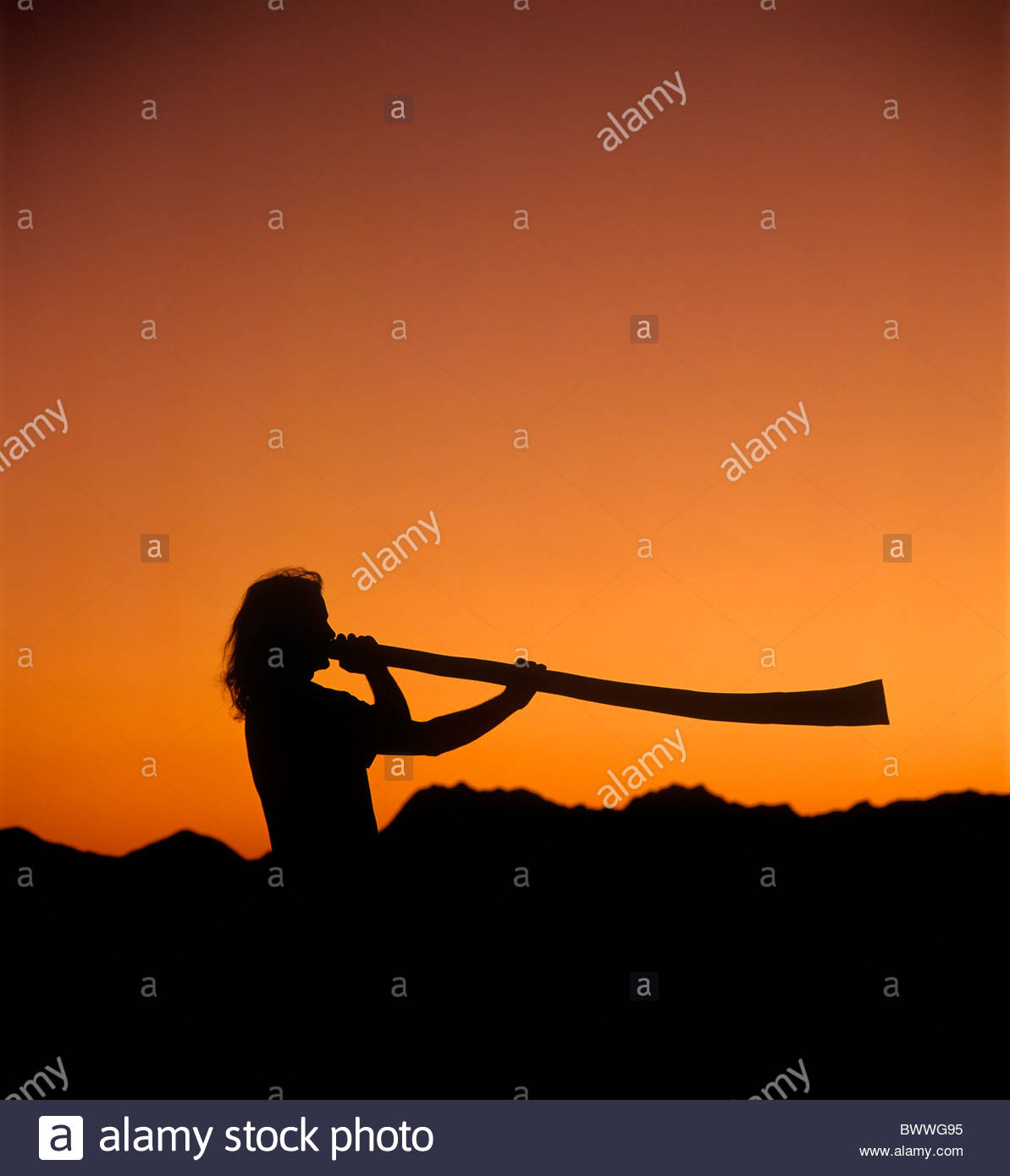 L'uomo gioca un didgeridoo al tramonto con le montagne di Tucson in silhouette di sfondo arancione e nero Foto Stock