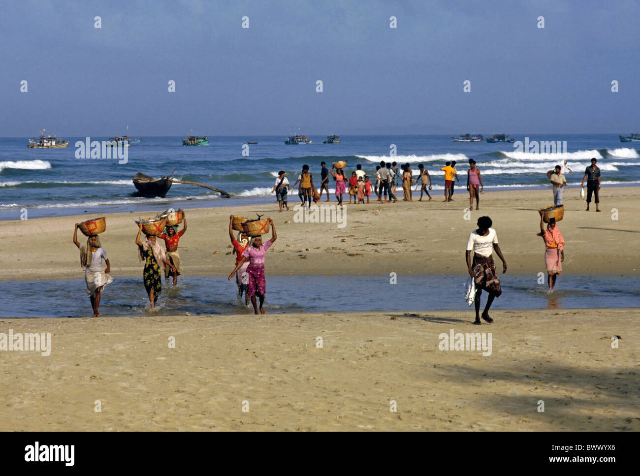 Uomo e donna che trasportano cesti di pesce torna da barche da pesca all'alba, Colva Beach, Goa, India. Foto Stock