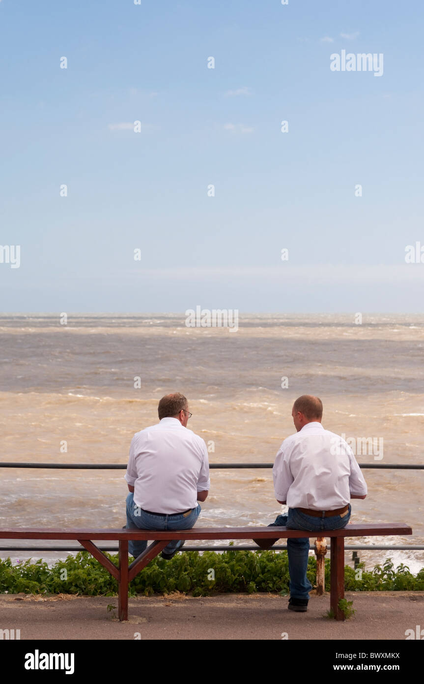 Due uomini sedersi e parlare su un banco di mare che si affaccia sul mare in Southwold , Suffolk , Inghilterra , Gran Bretagna , Regno Unito Foto Stock