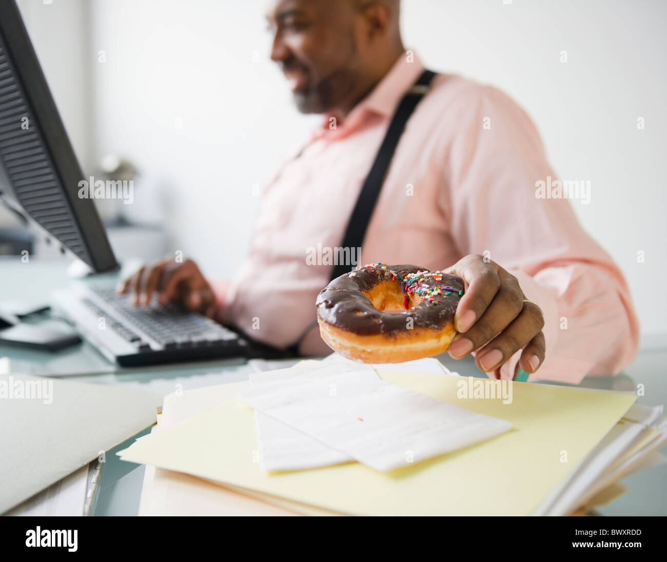 African American imprenditore ciambella di mangiare alla scrivania Foto Stock