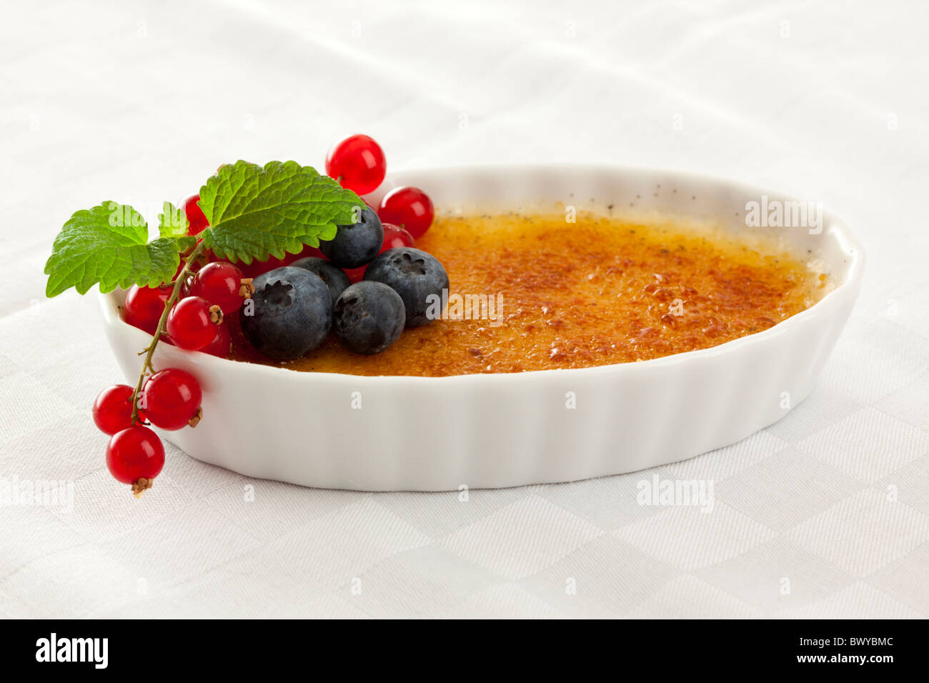 Tradizionale francese dessert creme brulee guarnita con frutti di bosco snd foglia di menta Foto Stock