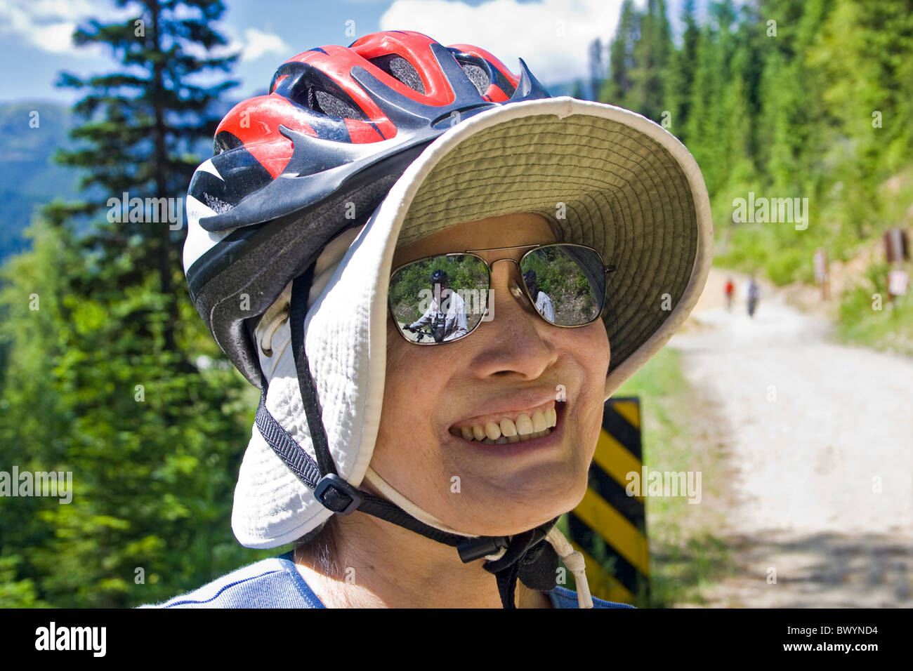 Donna ciclista indossando un floppy cappello per il sole sotto il casco per  bicicletta ha un compagno ciclista si riflette nei suoi occhiali da sole  sul sentiero di Hiawatha Foto stock -