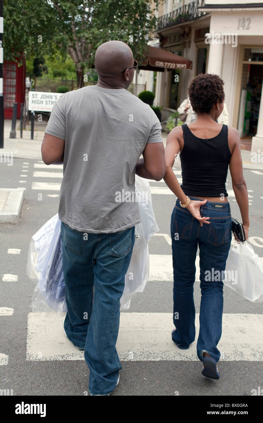 Coppia giovane portando la loro pulitura a secco e di shopping, tramite un passaggio pedonale a Londra il St John's Wood. DAVID MANSELL Foto Stock