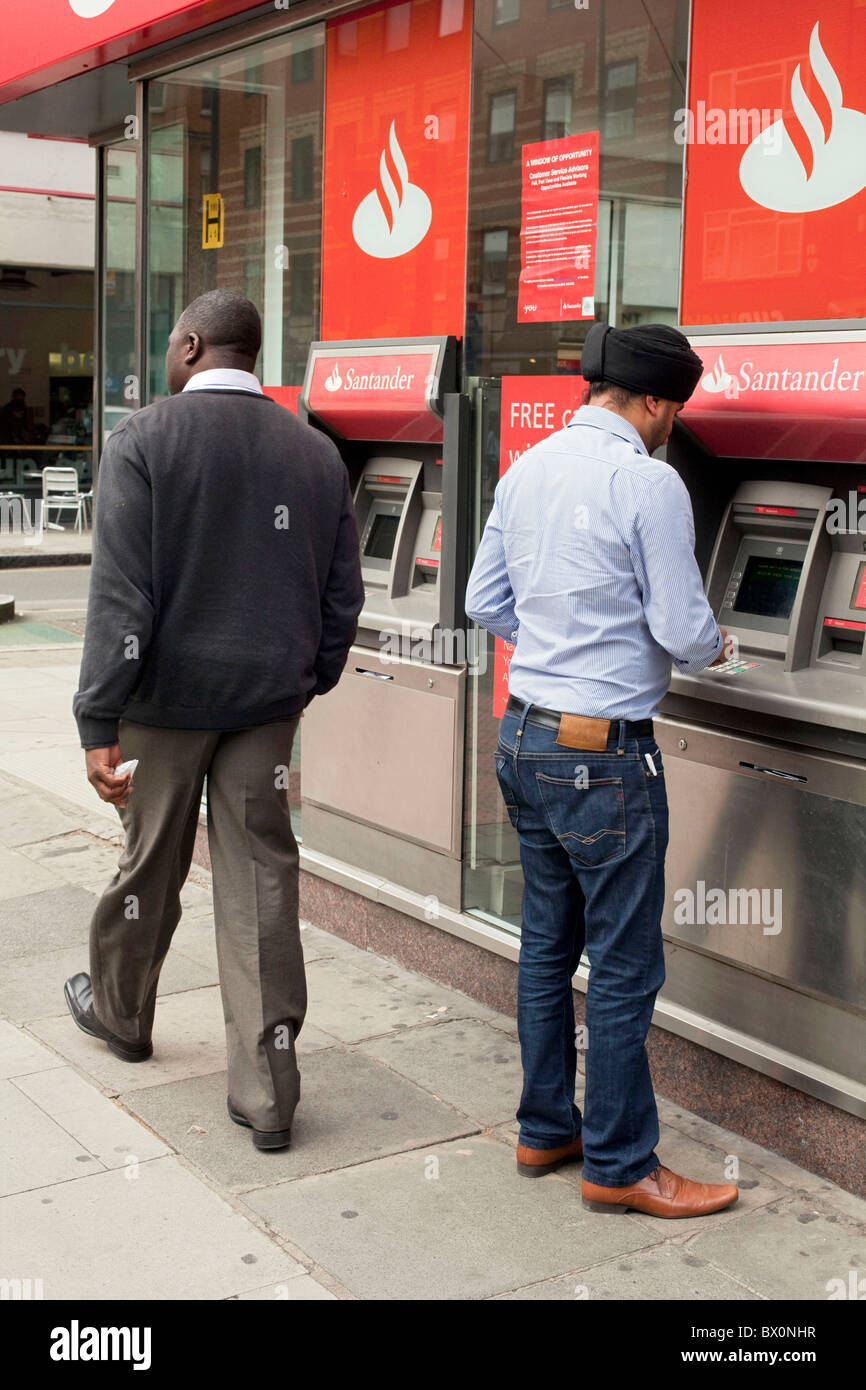 Un giovane uomo Sikh utilizzando una banca Santander ATM cash dispenser a Londra centrale. DAVID MANSELL Foto Stock